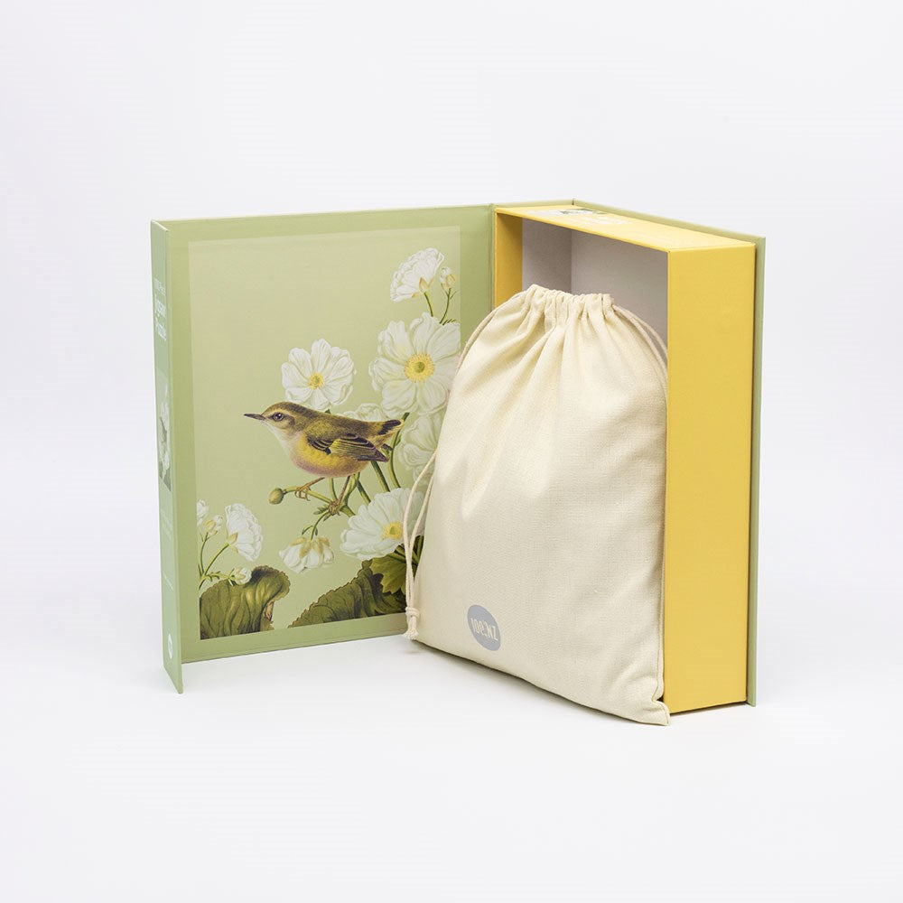 A fabric drawstring bag rests in the open Rifleman Jigsaw Puzzle Box, which features a Rifleman bird and white Mt Cook Lilly flowers on the inner cover, all set against a plain white background.
