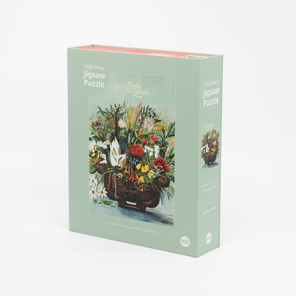 The NZ Native Flowers Jigsaw Puzzle Box is a rectangular box containing 1000 pieces, featuring vibrant New Zealand native flowers in a basket. The green box displays the image and text on both the front and side.