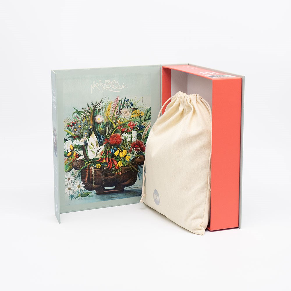 The NZ Native Flowers Jigsaw Puzzle Box features an illustrated cover with native flowers and opens to reveal a cloth drawstring bag nestled inside on the right of the package.