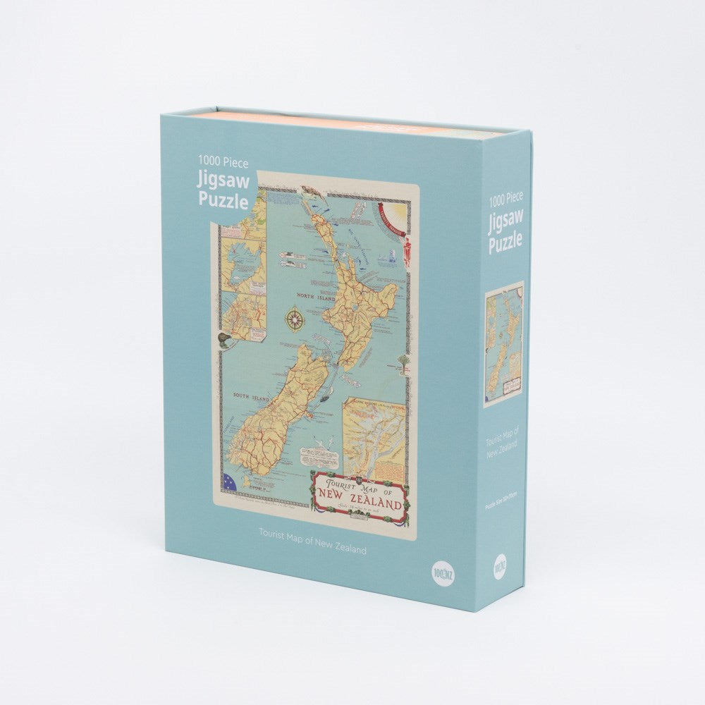 The Tourist Map of NZ Jigsaw Puzzle Box, in light blue, stands upright against a plain white background. The box features an image of its 1000-piece vintage New Zealand tourist map puzzle on the front.