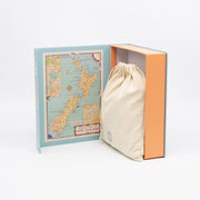 The Tourist Map of NZ Jigsaw Puzzle Box features a blue and orange box with a vintage New Zealand map inside the cover, plus a beige drawstring cloth bag—ideal for any New Zealand jigsaw puzzle enthusiast.