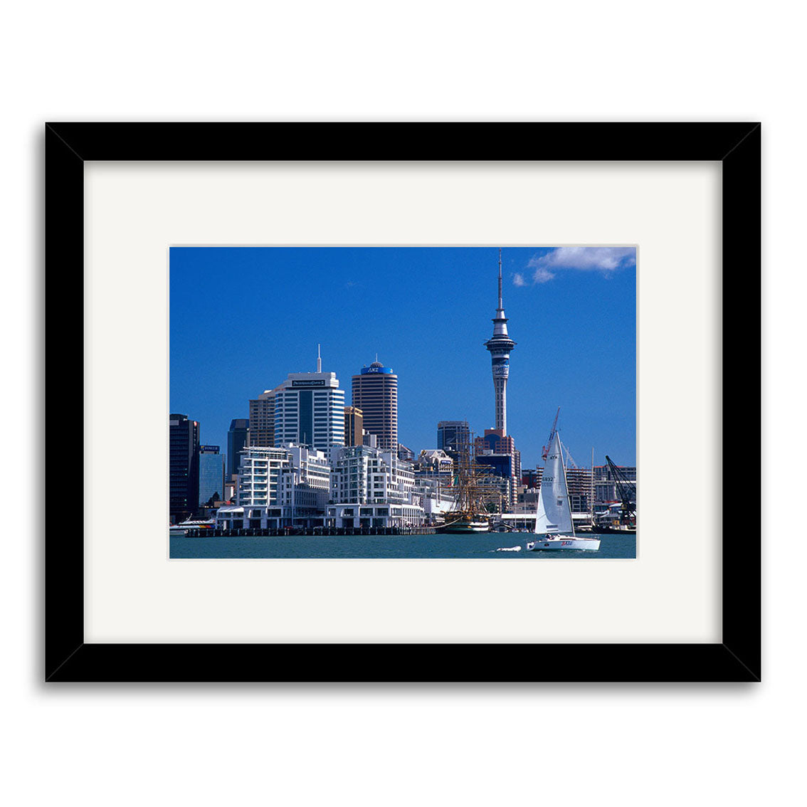 Auckland City - RP005: Framed photo of Aucklands skyline with modern buildings, a tall tower, and a sailboat on the water under a clear blue sky, printed on archival quality paper for lasting beauty.