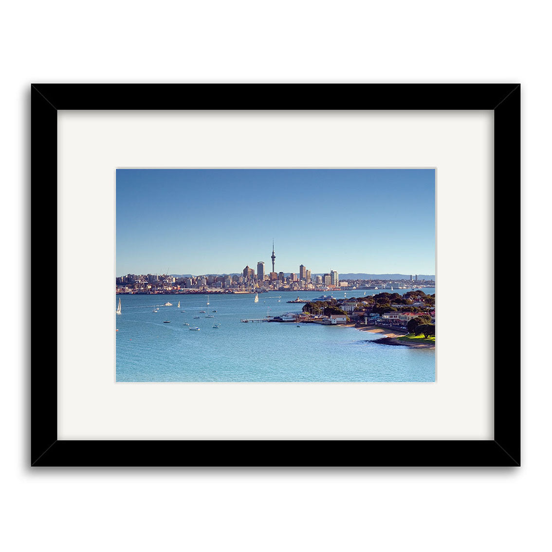Devonport - RP006 features a city skyline with a prominent tower, sailboats, and clear blue sky. Printed on archival matte paper, this New Zealand photographic print comes framed in black with a white mat.