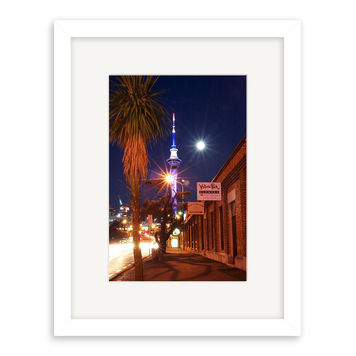 The Victoria Park - RP008 framed photographic print on archival matte paper features a nighttime New Zealand city street with a lit tower, palm tree, brick buildings including Viaduct Bar, and a bright moon in the dark sky.
