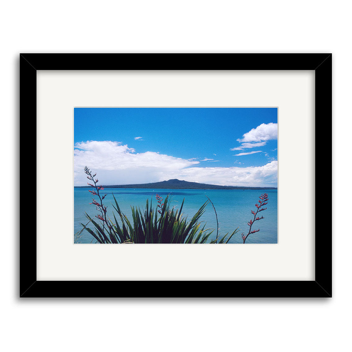 The Rangitoto Island - RP012 framed print features New Zealands blue ocean, a distant volcanic island, bright sky, and foreground plants with long green leaves and red flowers, printed on archival quality matte paper.