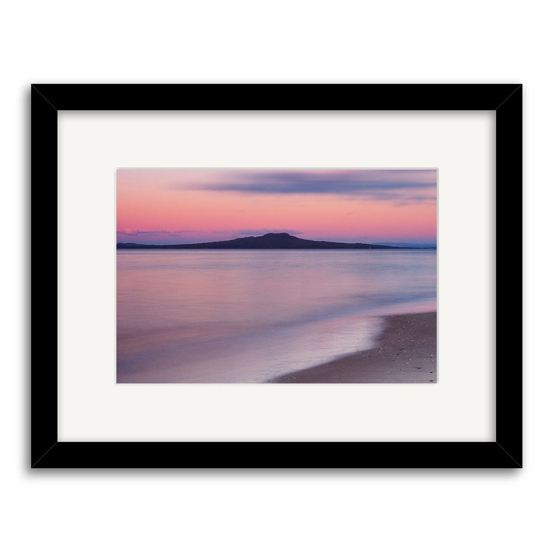 Takapuna Sunset - RP013 is a framed archival photograph of a peaceful New Zealand beach at sunset, featuring soft pink and purple skies reflecting on the water with a distant island or mountain silhouette on the horizon.