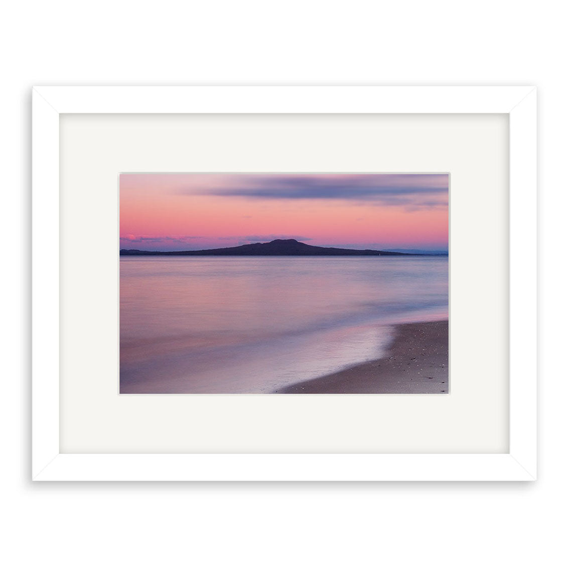 Takapuna Sunset - RP013 is a framed photographic print featuring a calm New Zealand beach at sunset, with soft pink and purple tones and an island silhouette. A white frame with wide mat adds elegance to this archival quality piece.