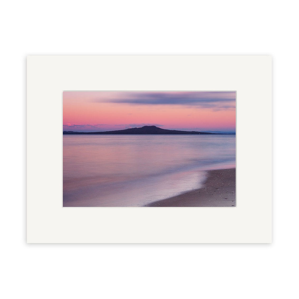 A framed archival quality print titled Takapuna Sunset - RP013, featuring a calm New Zealand beach at sunset with gentle waves, an island in the distance, and a pink-purple sky.