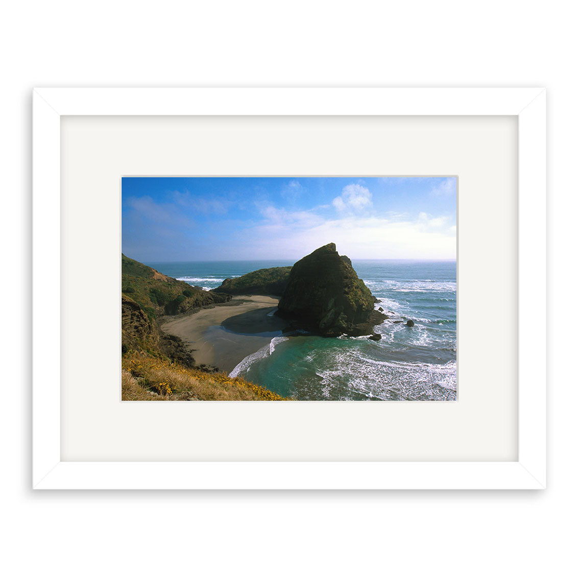 Piha South - RP017: A framed photograph featuring New Zealand’s rocky coastline, sandy beach, ocean waves, and blue sky. Centered in a white mat and archival-quality matte paper frame.