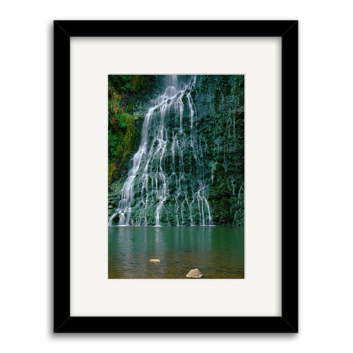 Framed archival quality photographic print, Karekare Waterfall - RP018, featuring a New Zealand waterfall cascading over a lush, rocky cliff into a tranquil pool. Presented centered within a white mat and black frame.