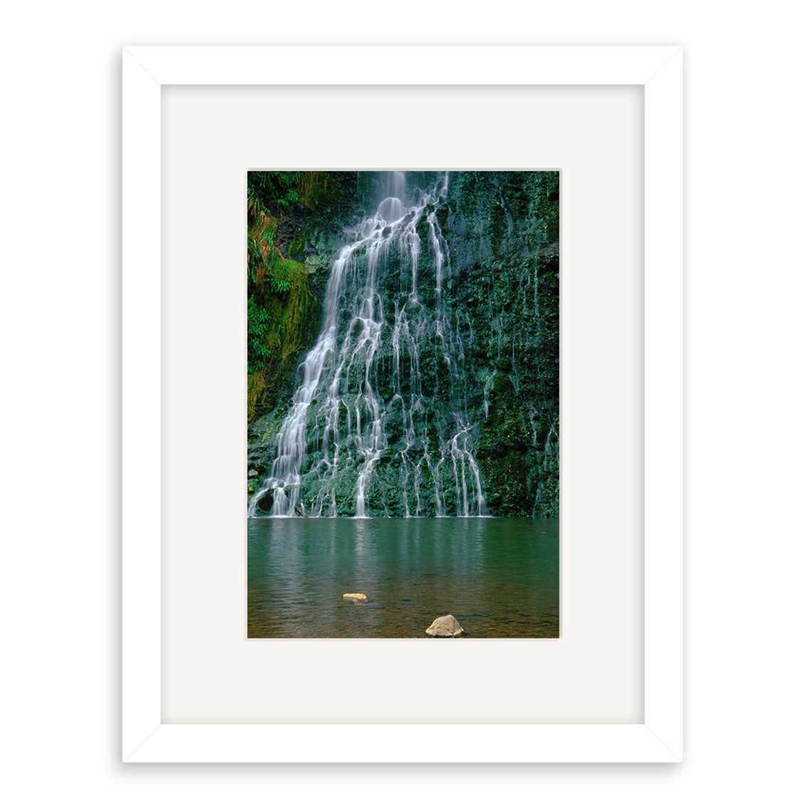 Karekare Waterfall - RP018 features a framed photograph capturing New Zealand’s Karekare Waterfall cascading over a mossy cliff into a calm pool. The white frame and mat highlight the archival print, with rocks visible near the water’s surface.