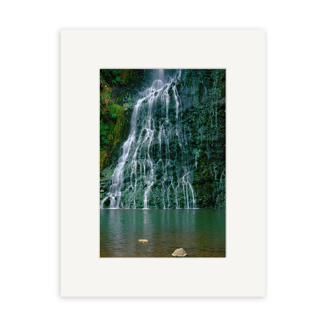 The Karekare Waterfall - RP018 is a framed photographic print featuring a New Zealand waterfall flowing over rocks into a green pool, with lush vegetation and three prominent rocks in the water. This is an archival-quality image.