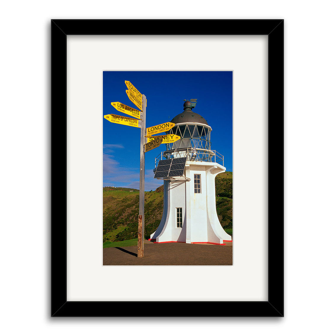 Cape Reinga Lighthouse - RP024 features a white tower with solar panels and a glass lantern near yellow direction signs, set against New Zealand’s blue sky—perfect for photographic prints on archival quality matte paper.