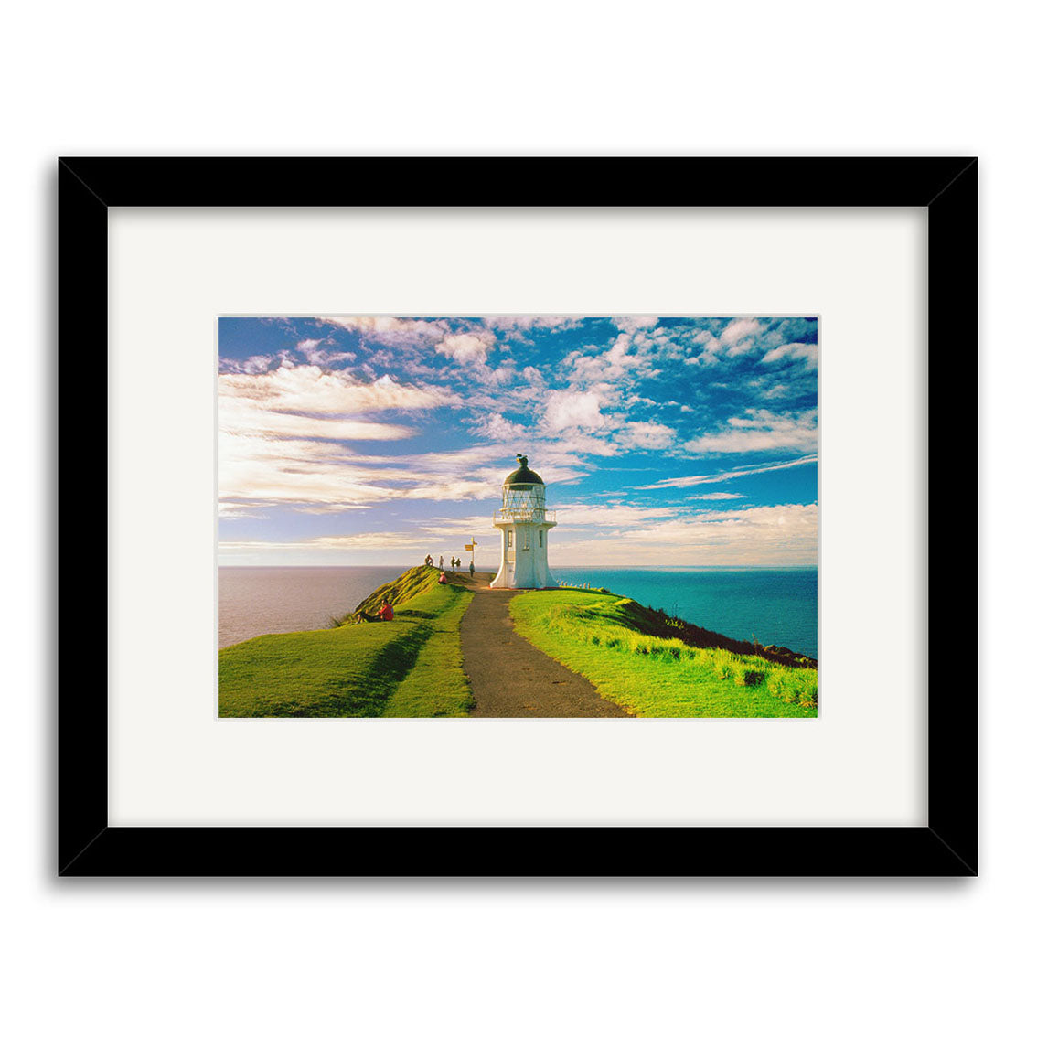 Cape Reinga - RP025: A framed archival photo of a white lighthouse on a grassy New Zealand cliff by the ocean, featuring a path under a partly cloudy blue sky.
