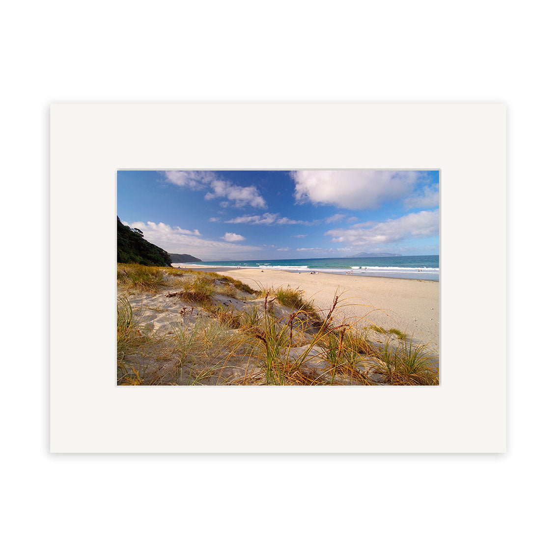 Mangawhai Beach - RP032: A sandy beach with grassy dunes and waves under a blue sky. This New Zealand scene comes with a white mat frame and is available as archival quality photographic prints.