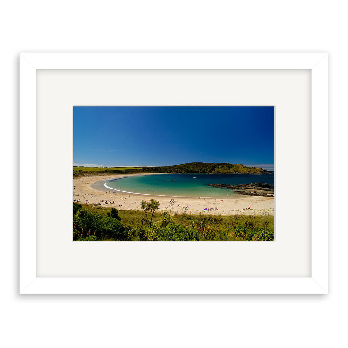 A framed photographic print, Matai Bay – RP033, features a sandy beach with clear blue water, a few people sunbathing and swimming, and green hills under a clear sky, printed on archival quality matte paper.