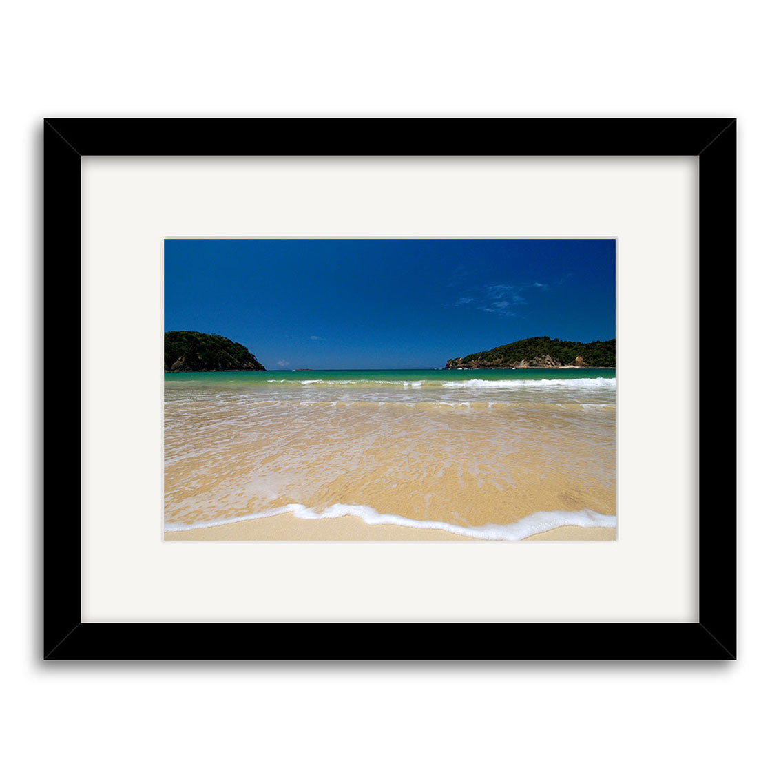 Matapouri - RP034: Framed photographic print featuring a sandy beach, gentle waves, clear blue water, deep blue sky, and distant green hills. Centered image with white mat in a black frame on archival quality matte paper.