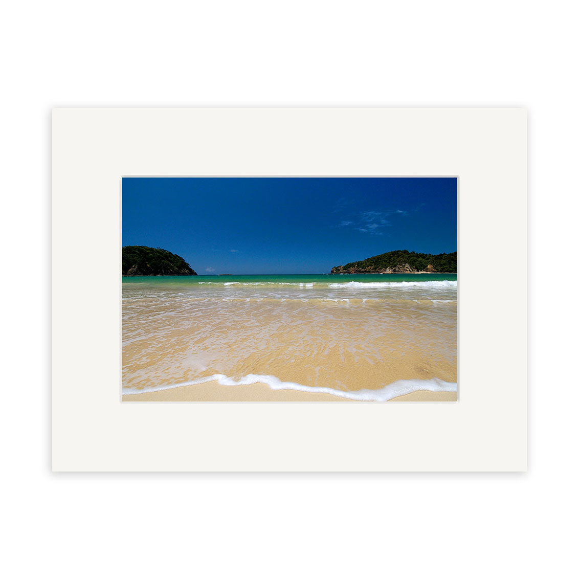 Matapouri - RP034 features a sandy beach with gentle waves, green hills, and a clear blue sky in New Zealand. The image is centered within a white mat frame and printed on archival quality matte paper.