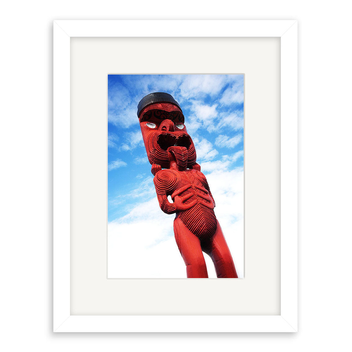 The Maori Statue - RP041 features a framed photo of a red Māori carving with intricate patterns and large eyes against a blue sky. Available as archival quality photographic prints.