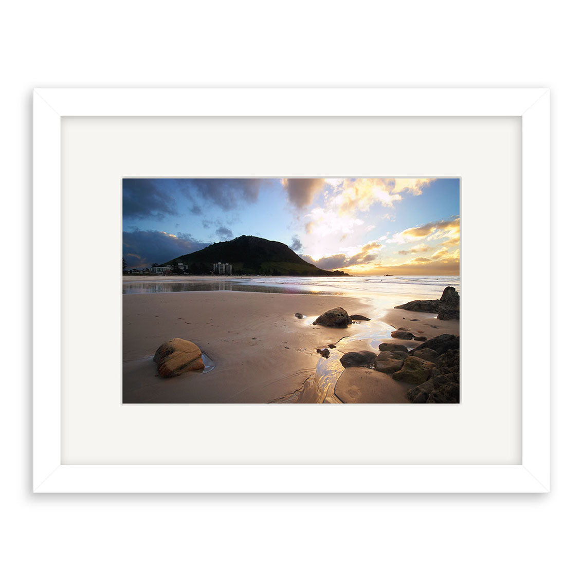 Mt Maunganui - RP043: A framed photographic print featuring a sandy New Zealand beach at sunrise or sunset, rocks in the foreground, water reflecting the sky, and a green hill—beautifully rendered on archival quality matte paper.