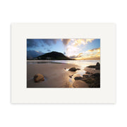 Mt Maunganui - RP043: A sunset beach in New Zealand with rocks, wet sand reflecting the sky, hills and buildings beyond, and sunlight through clouds—available as photographic prints on archival quality matte paper.