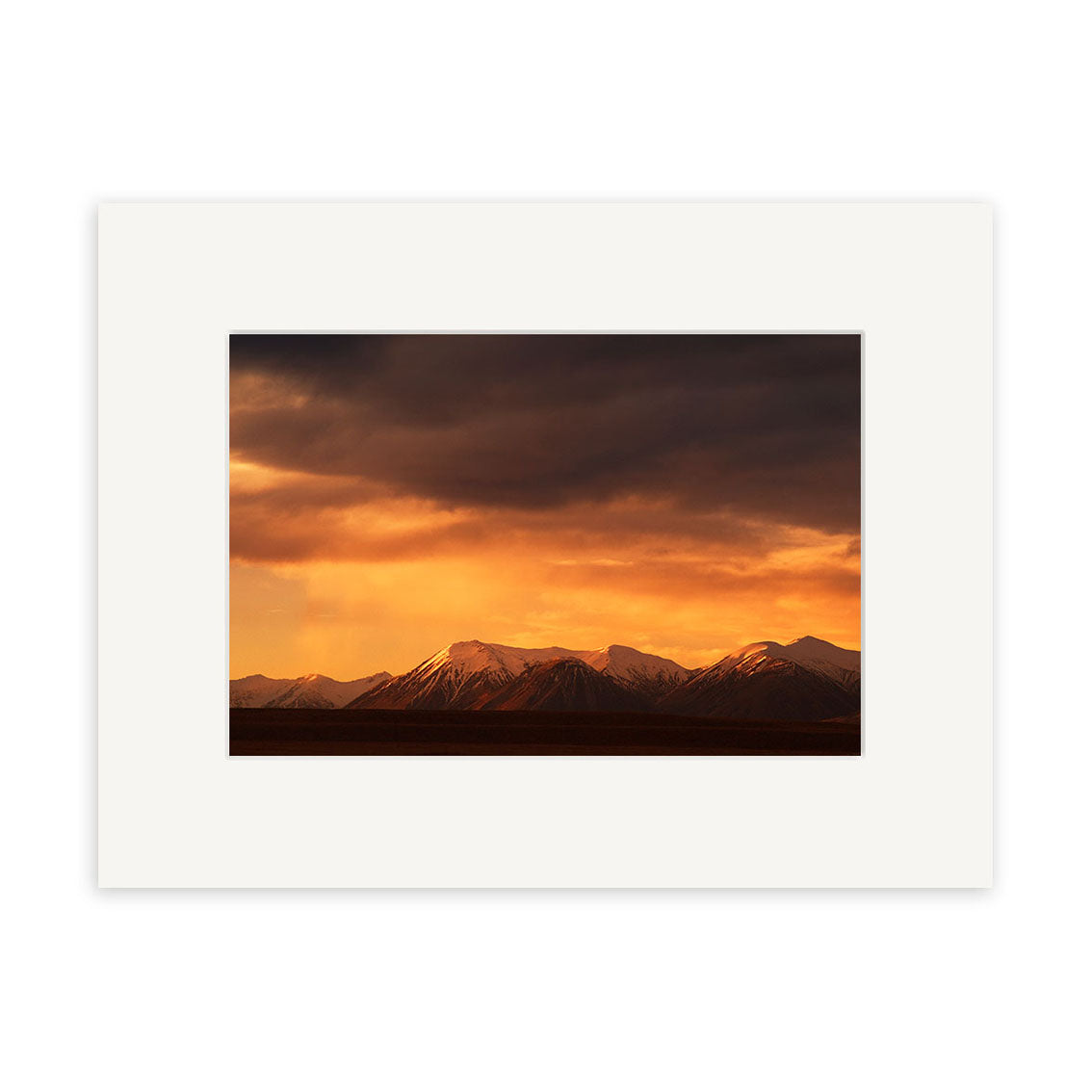 Southern Alps - RP049: A dramatic sunset photograph of New Zealands snow-capped mountains, orange and dark clouds above. Printed on archival matte paper with a white mat border—perfect for showcasing photographic art.