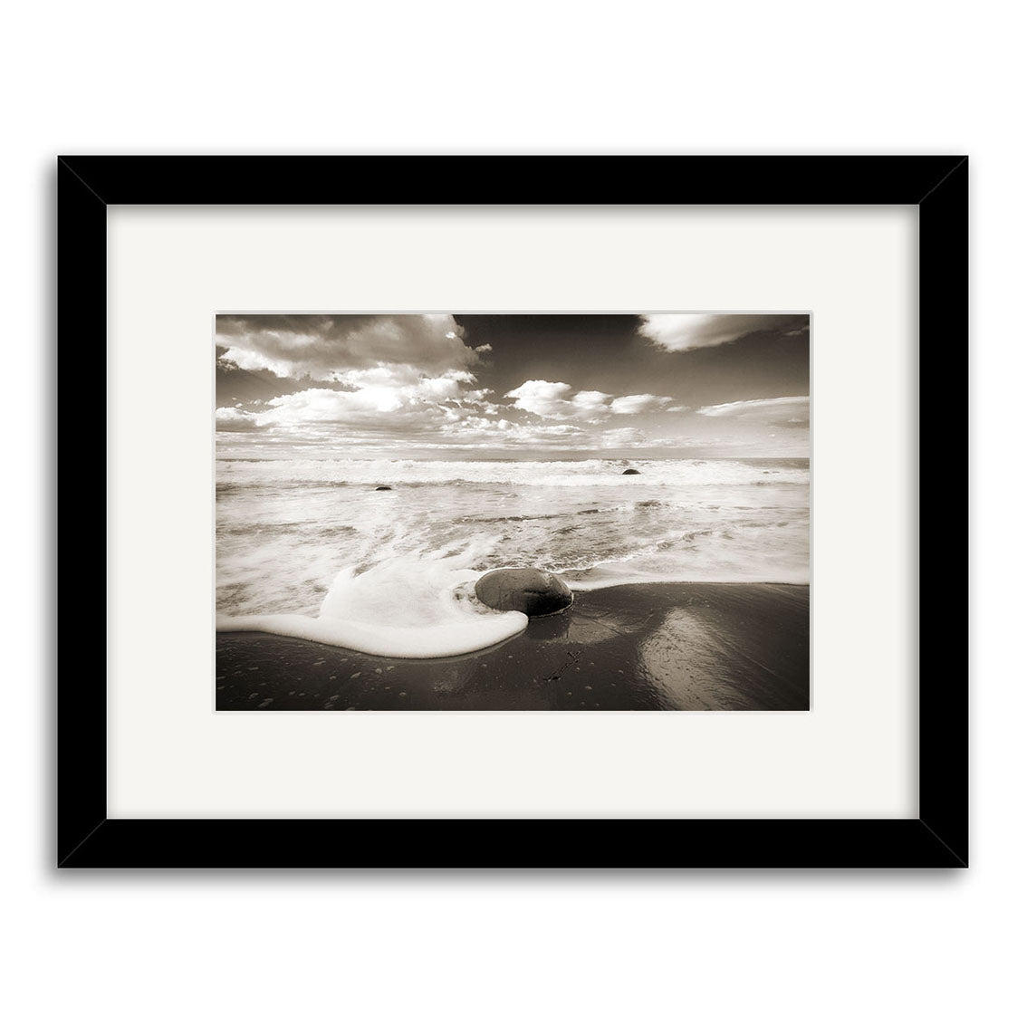 Moeraki Boulders - RP055: A black-and-white framed photo of a beach scene with a round boulder, waves ashore, and cloudy sky. Printed on archival paper for lasting beauty.