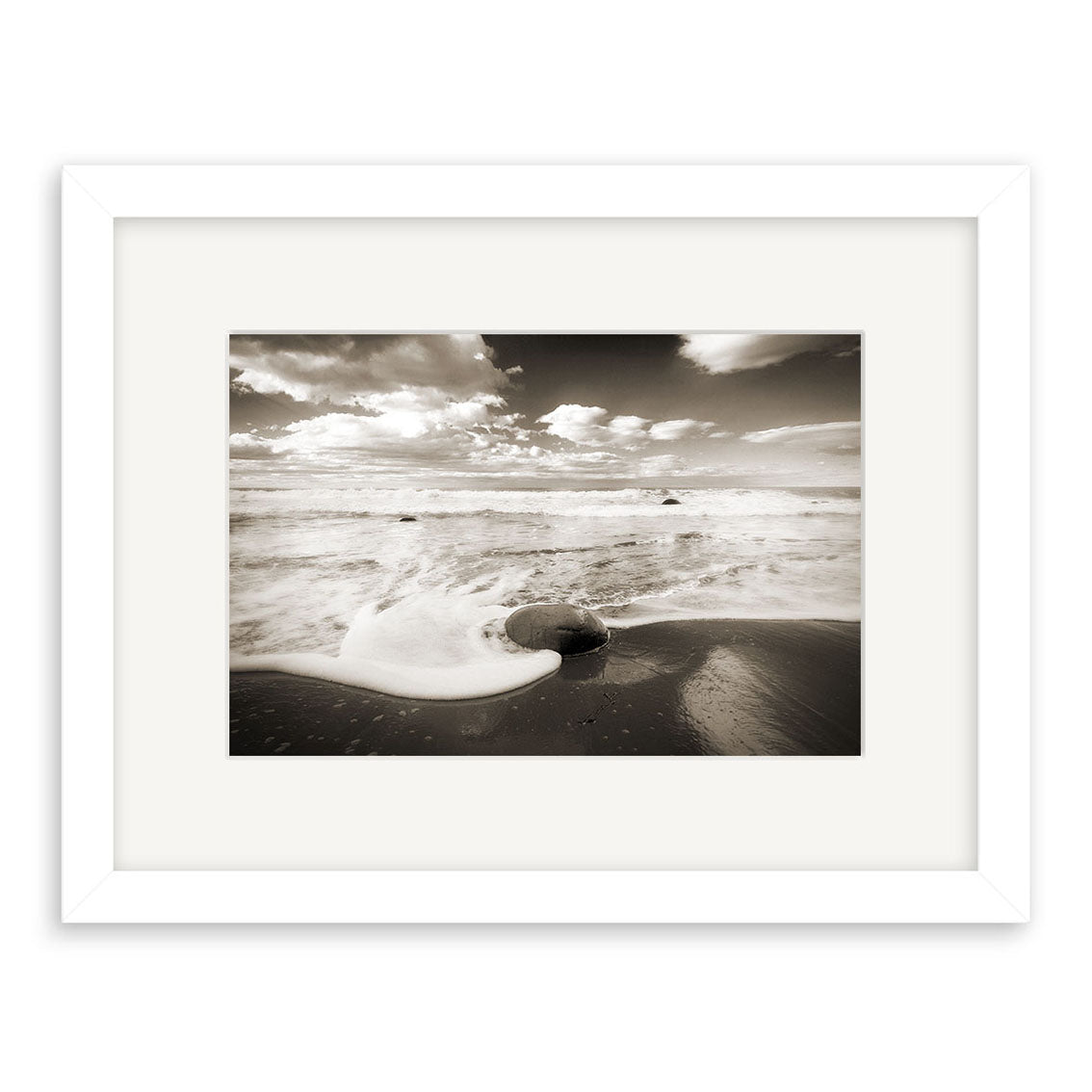 Moeraki Boulders - RP055: A framed black and white photo of ocean waves over a large rock on a sandy New Zealand beach, with cloud-filled skies. Printed on archival quality paper—ideal for fine art photography enthusiasts.