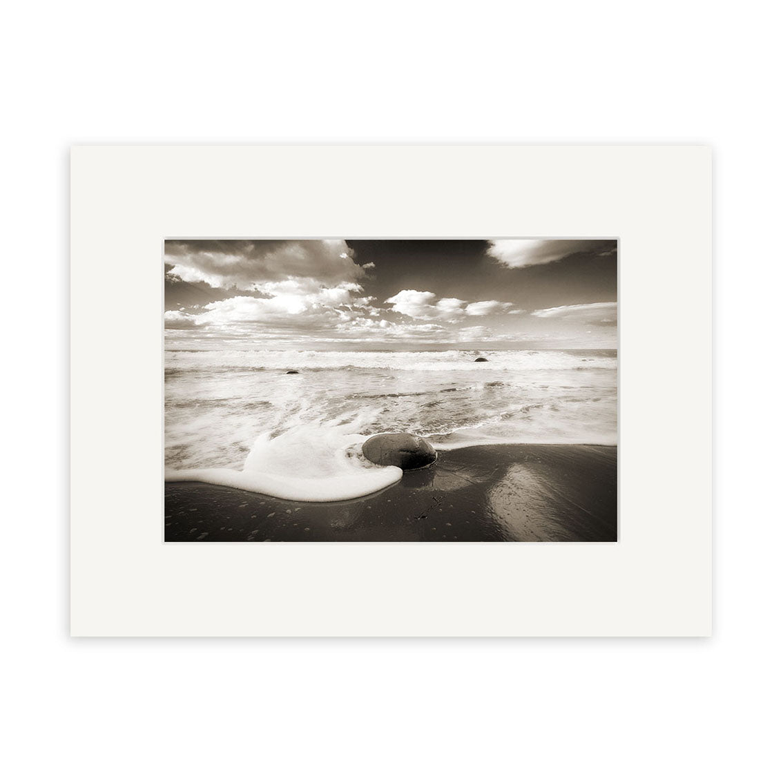 Moeraki Boulders - RP055: Black and white photo of ocean waves washing over a large round boulder on a New Zealand beach, with distant horizon, clouds, and a white border—ideal for photographic prints.