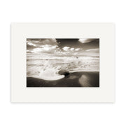Moeraki Boulders - RP055: Black and white photo of ocean waves washing over a large round boulder on a New Zealand beach, with distant horizon, clouds, and a white border—ideal for photographic prints.