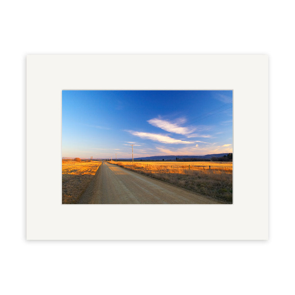 A dirt road winds through golden fields beneath a blue sky in Wedderburn - RP057 by Reuben Price, available as archival quality matte paper New Zealand photographic prints.