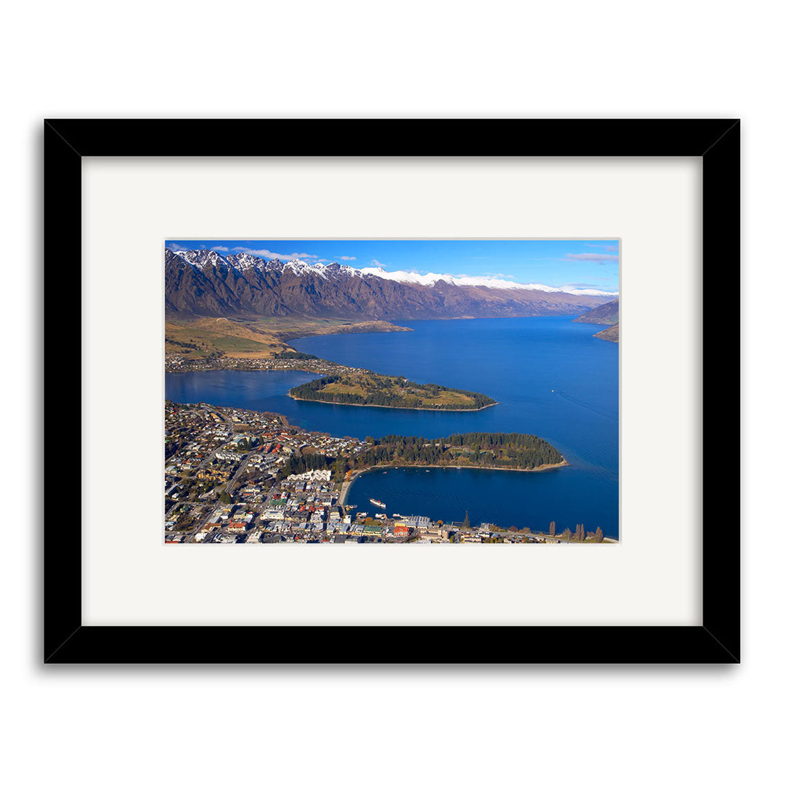 Queenstown - RP063: Framed photograph of a lakeside New Zealand town by a blue lake, with forested peninsulas and snowy mountains under a clear sky. Available as photographic prints on archival quality matte paper.