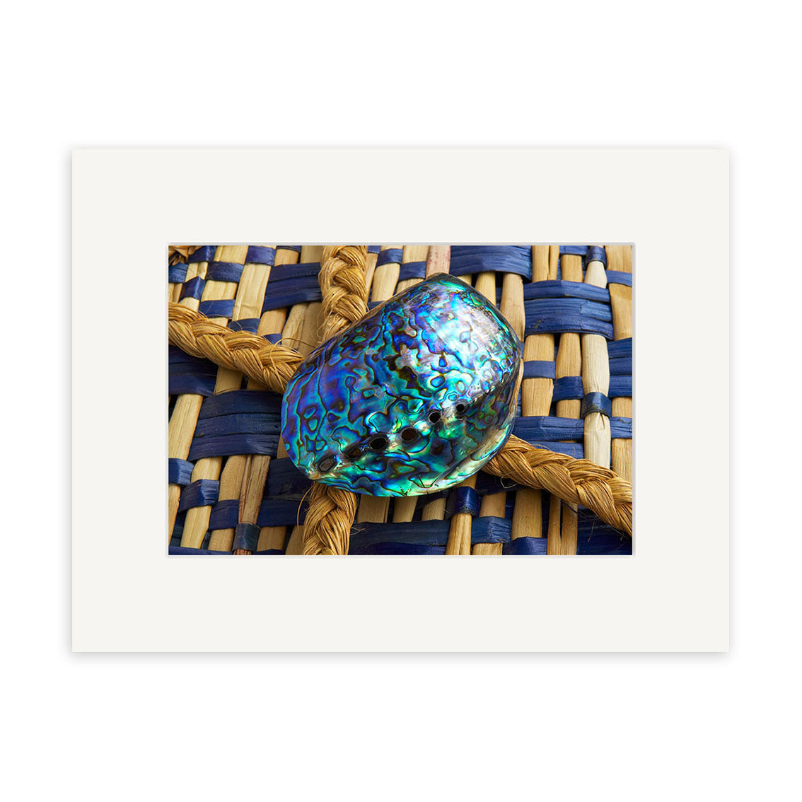 A close-up of the Paua Shell - RP085, iridescent and resting on a tan and navy woven surface, is showcased within a white mat—ideal for photographic prints on archival quality matte paper.