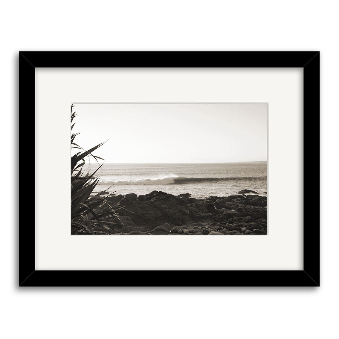 Whale Bay - RP091: Black and white photo of ocean waves on New Zealands rocky shore, plants in foreground. Framed in black with white mat, printed on archival-quality paper for lasting, stunning results.
