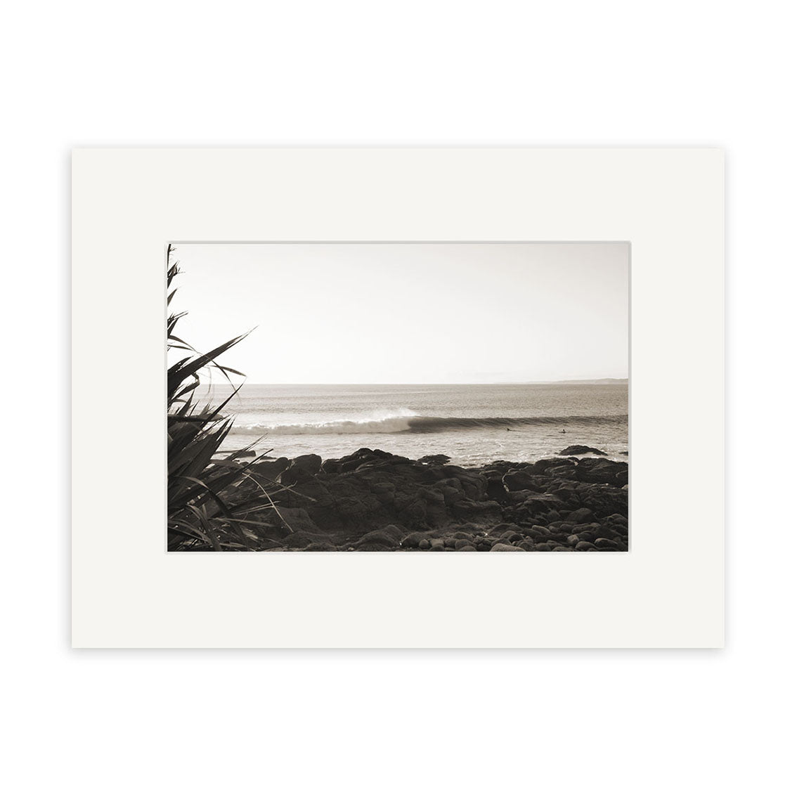 Whale Bay - RP091: A black and white photo of waves crashing on New Zealand rocks, with foreground plants. Set in a white mat frame and printed on archival quality paper for stunning photographic prints.