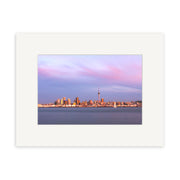 The Auckland Twilight Skyline - RP092 is a framed photographic print of Auckland’s city skyline at sunset, with tall buildings, a prominent tower, pastel purple-pink skies, calm water, and archival-quality craftsmanship for lasting beauty.