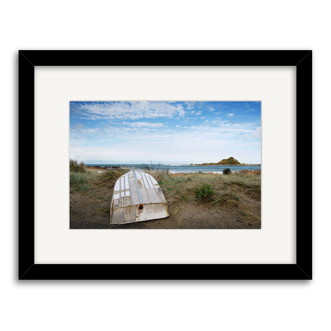 Island Bay 2 - RP107 is a framed photographic print by Reuben Price, featuring an old rowboat on sandy grass overlooking the New Zealand ocean, with a distant island visible under a partly cloudy sky.