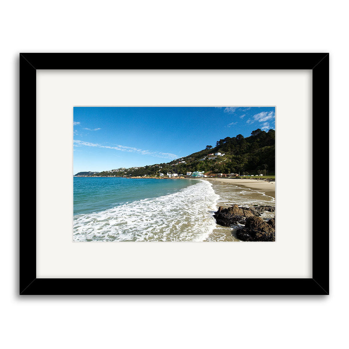 Scorching Bay - RP109: A framed coastal New Zealand photo with waves on sandy beach, rocks in front, and houses under a blue sky—printed on archival quality matte paper.