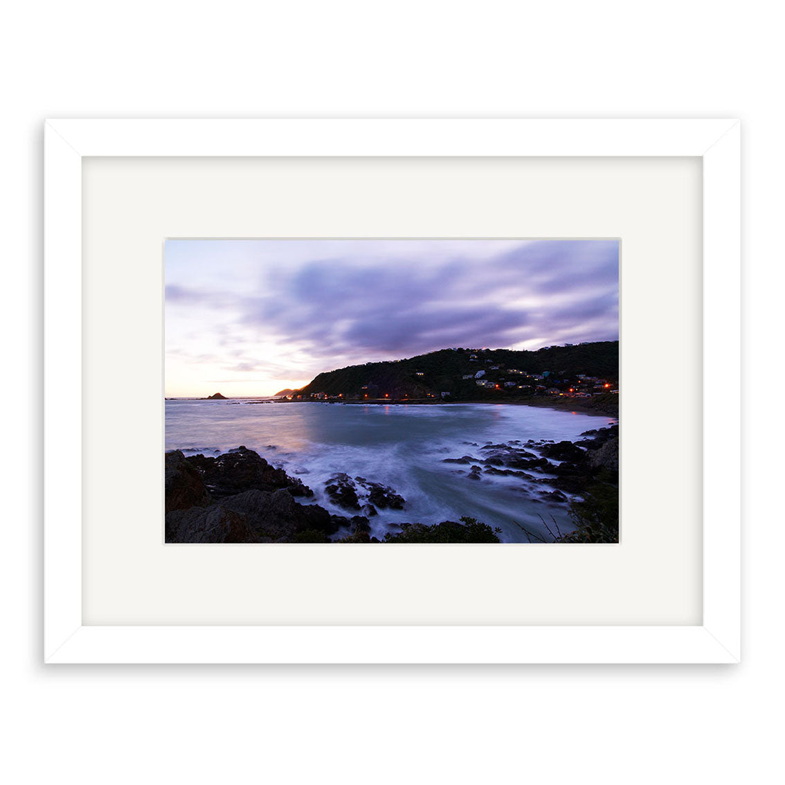 Framed archival quality print, Houghton Bay - RP112 by Reuben Price: a rocky coastline at dusk with waves onshore and hillside house lights beneath a cloudy sky.
