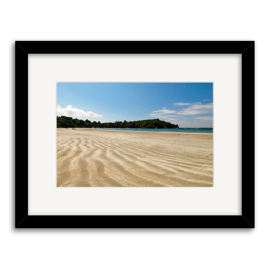 A framed photographic print titled Oneroa Beach - Waiheke - RP115, featuring sandy ripple patterns, a green headland, and blue skies. Printed on archival paper with a black frame and white mat. Inspired by New Zealand landscapes.