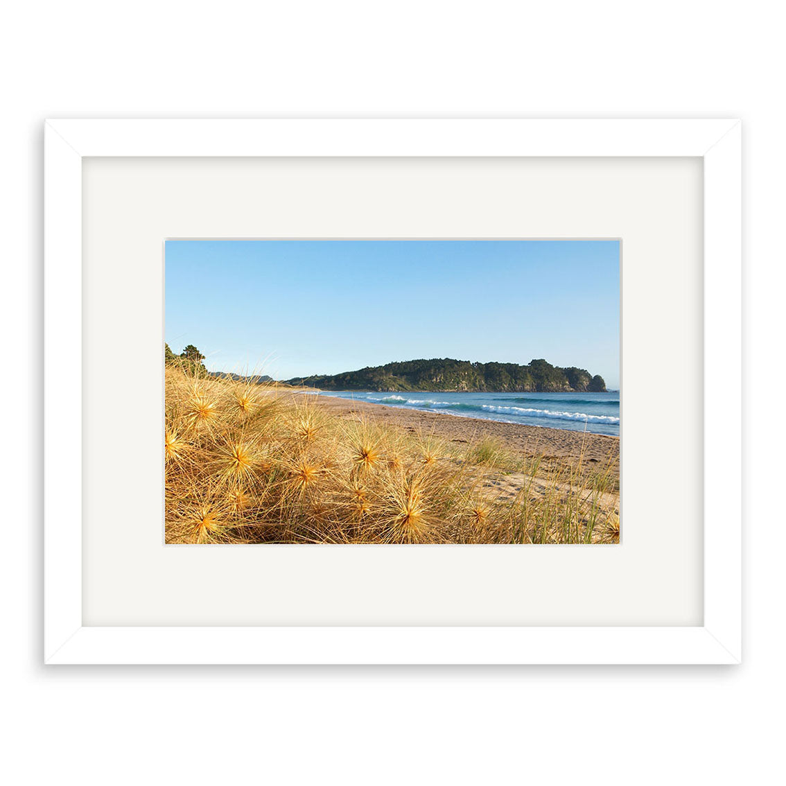 Hot Water Beach - RP123 is a framed photographic print by Reuben Price, showing dry grasses, rolling waves, and a tree-covered hill on archival matte paper under a clear blue sky.