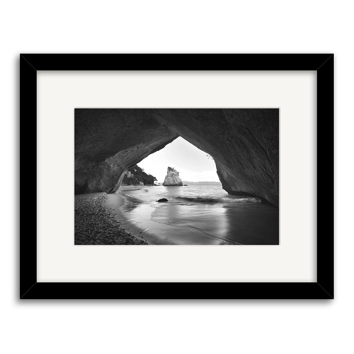 Cathedral Cove - RP125: Black and white photo of a coastal rock arch in New Zealand, framing the sea and an offshore rock. Printed on archival matte paper, it comes in a black frame with white mat.