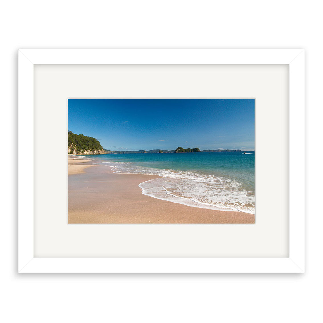 Hahei Beach - RP126: A framed print featuring a sandy beach, gentle waves, clear blue water, and a distant rocky coastline under a blue sky. Printed on archival matte paper with a white frame and wide mat.