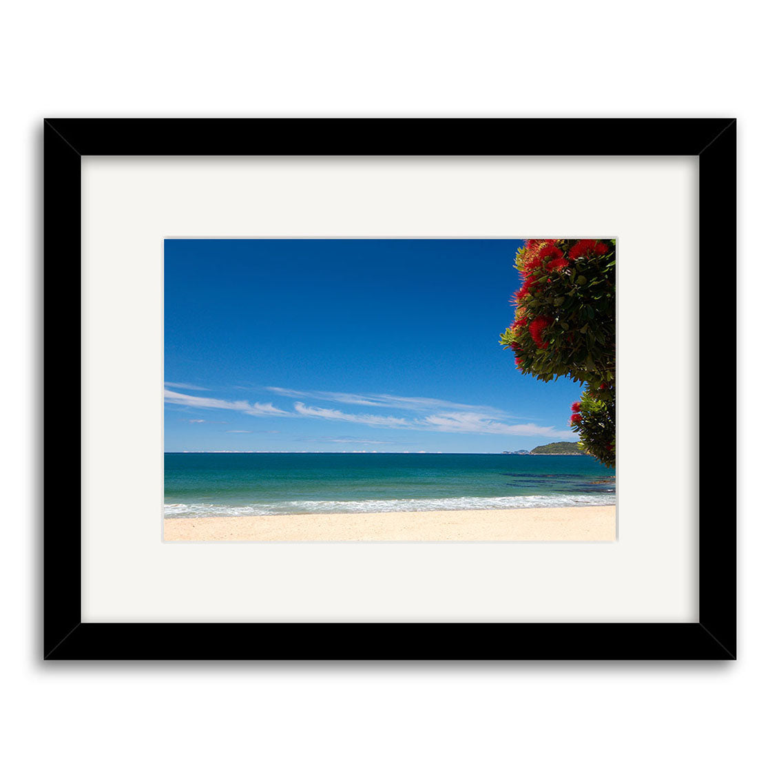 The Tairua - RP127 is a framed photographic print showcasing a sandy beach, turquoise ocean, and clear blue sky with red flowers and green foliage. Printed on archival-quality paper, it beautifully captures New Zealand’s coastline.