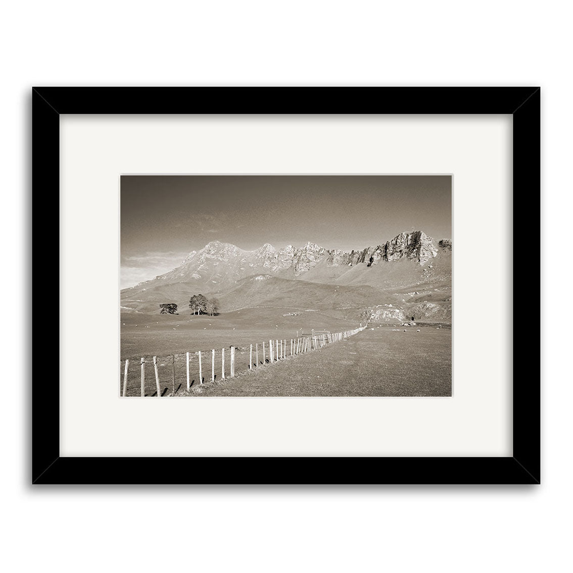 Te Mata Peak - RP132: A black-and-white framed photograph of a rural New Zealand landscape with a fence, grassy field, distant trees, and mountains. Centered in a white mat and black frame, printed on archival quality matte paper.