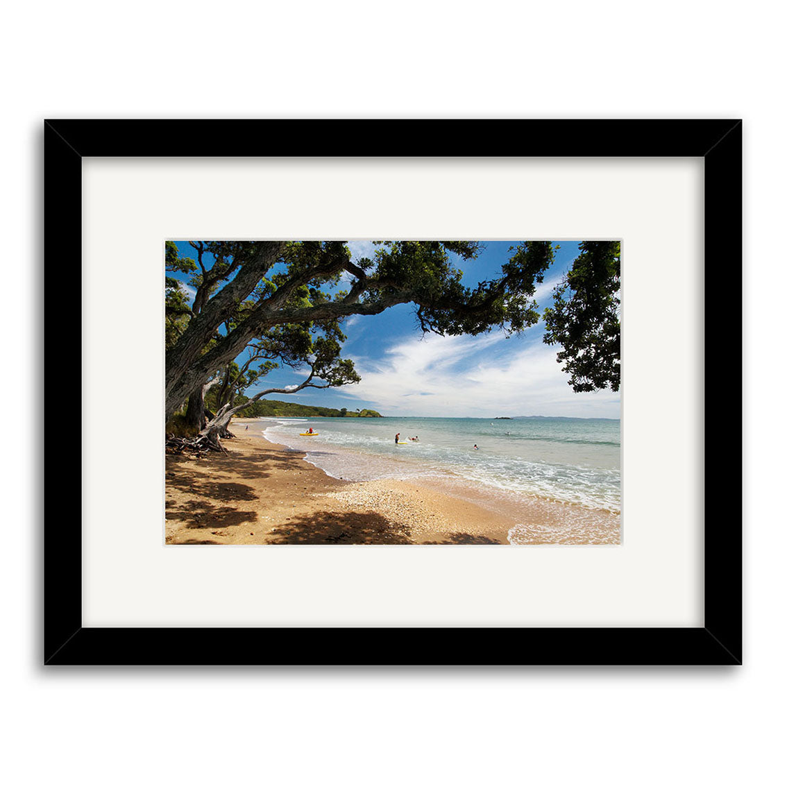 Coopers Beach - RP137: A framed photo of a sandy New Zealand beach with trees, swimmers in gentle waves, and a blue sky. Presented in a black frame with white mat on archival quality matte paper.