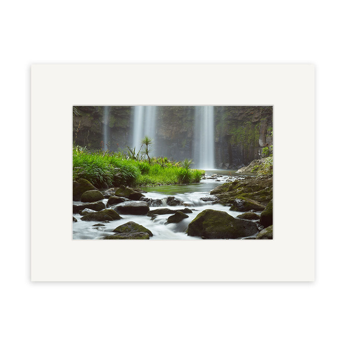Whangarei Falls - RP139: A photograph of a New Zealand waterfall with rocks, moss, and green grass along a flowing stream—available as archival quality prints with wide white mat.