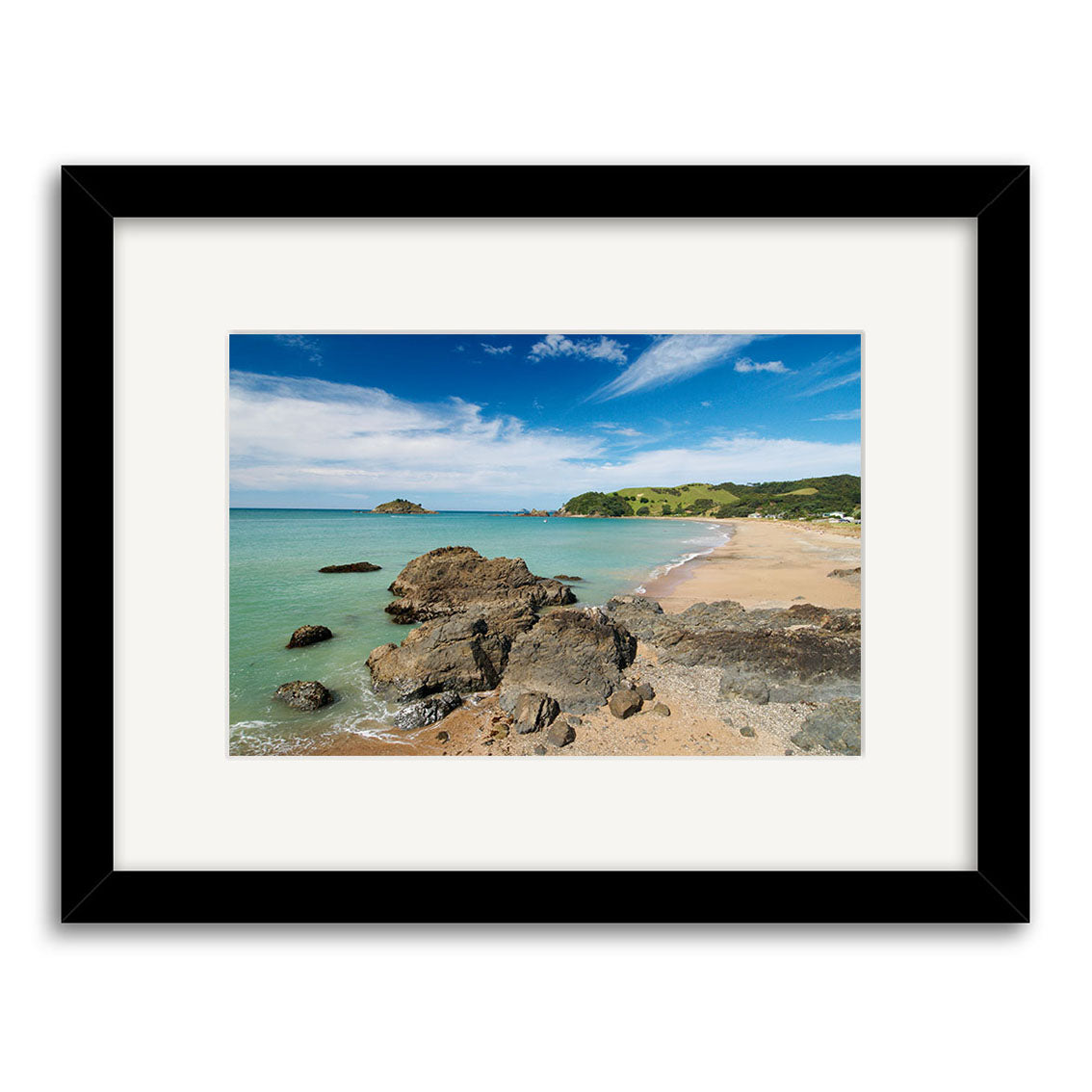 The Te Ngaire - RP140 is a framed photographic print of a New Zealand coastal landscape with rocky formations, sandy beach, green hills, and blue sky on archival-quality matte paper.