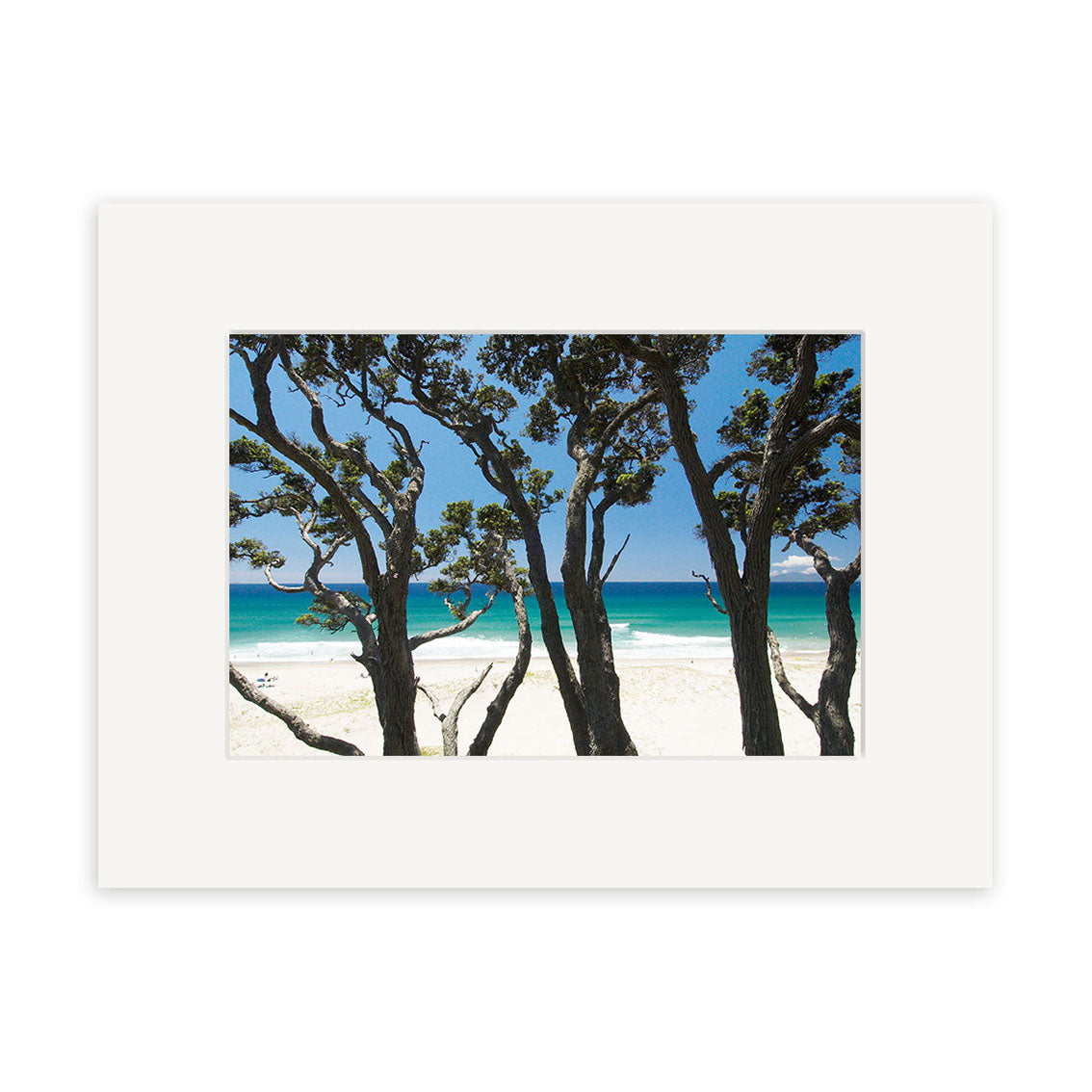 Pakiri Beach - RP143: A framed photo of a sandy New Zealand beach and turquoise ocean, viewed through tree silhouettes. Printed on archival matte paper and showcased in a white frame with simple matting.