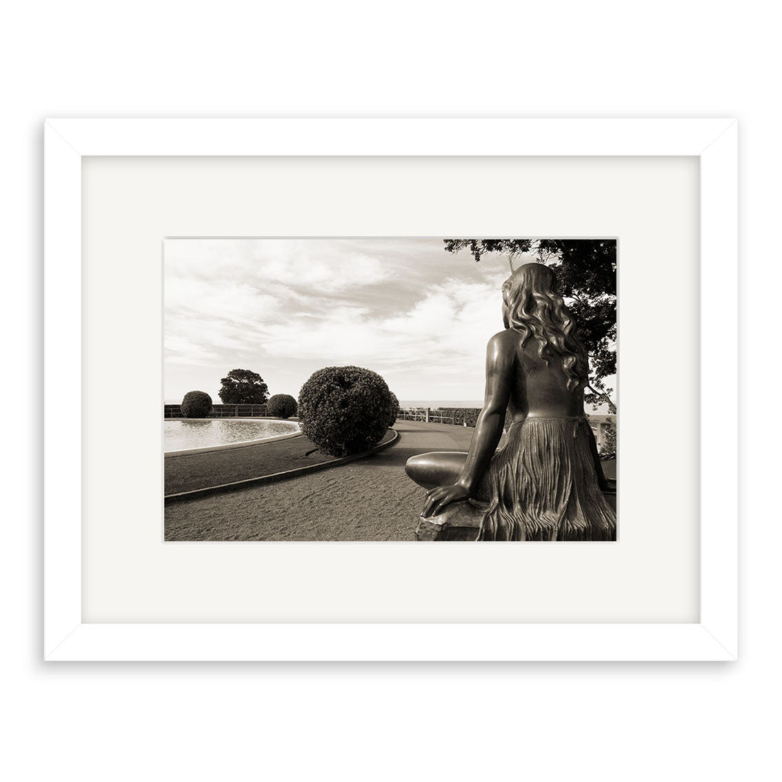 A framed archival black-and-white photo, Pania of the Reef - RP144, features a statue of a girl with long hair sitting on a ledge overlooking gardens, a round hedge, tree, and pool beneath New Zealand’s partly cloudy sky.